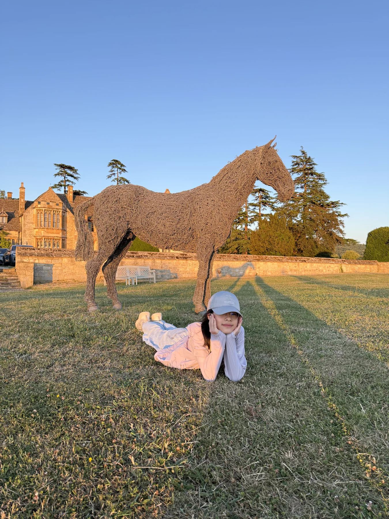 Angela relaxing on the grass beside a woven horse sculpture in the evening light